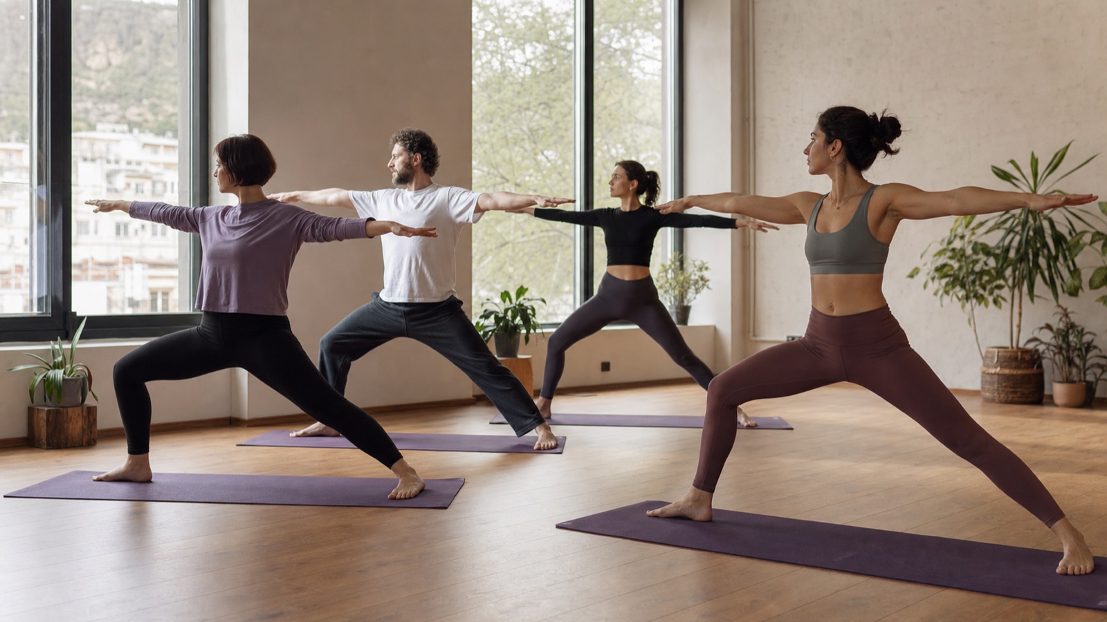 Cuatro adultos principiantes realizan la postura del guerrero de yoga en un estudio de Tbilisi con un instructor
